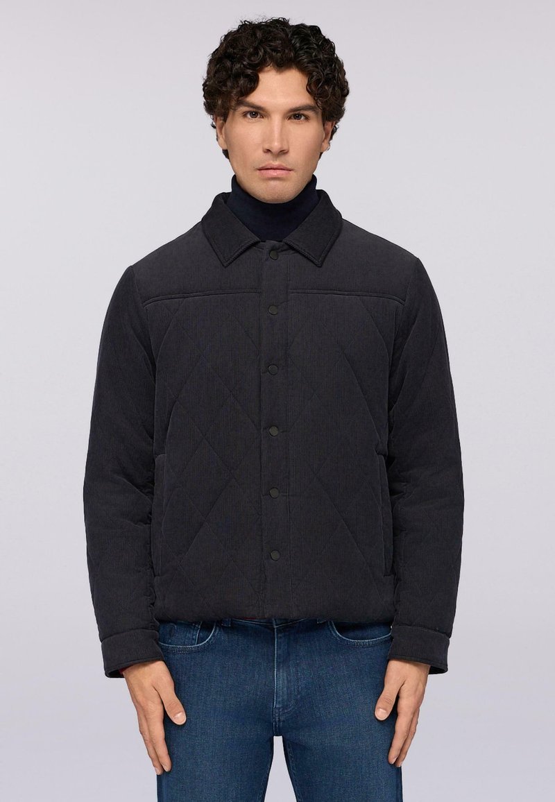 Quiltad mörkgrå jacka med krage, knäppning fram och textil med struktur, i kombination med blå denimjeans. Solitt utförande och modern passform.