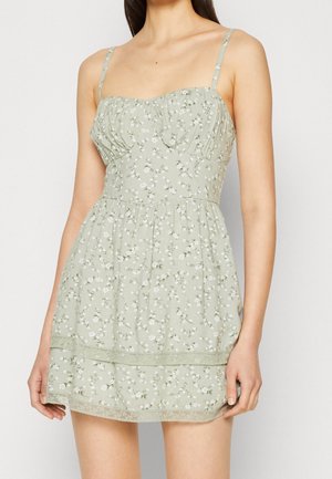 Lichtgroene bloemenjurk met dunne bandjes, geplooide taille en kanten rand aan de zoom. Gemaakt van zacht stof met een delicaat patroon.