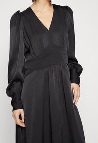 Svart klänning med V-ringning, puffärmar och figursydd midja. Tillverkad av ett strukturerat tyg med en flödande kjol.