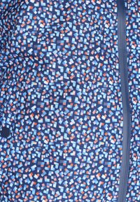 Giacca stampata con una base blu navy e forme geometriche multicolori. Il materiale sembra liscio, con una zip centrale e una tasca laterale.