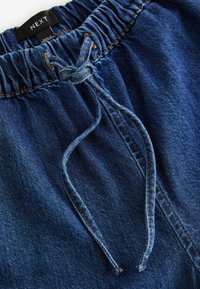 Denim-shortsit tummansinisellä pesulla, joissa on joustava vyötärö ja naru. Mukana näkyvät ompeluyksityiskohdat ja kangastagi.