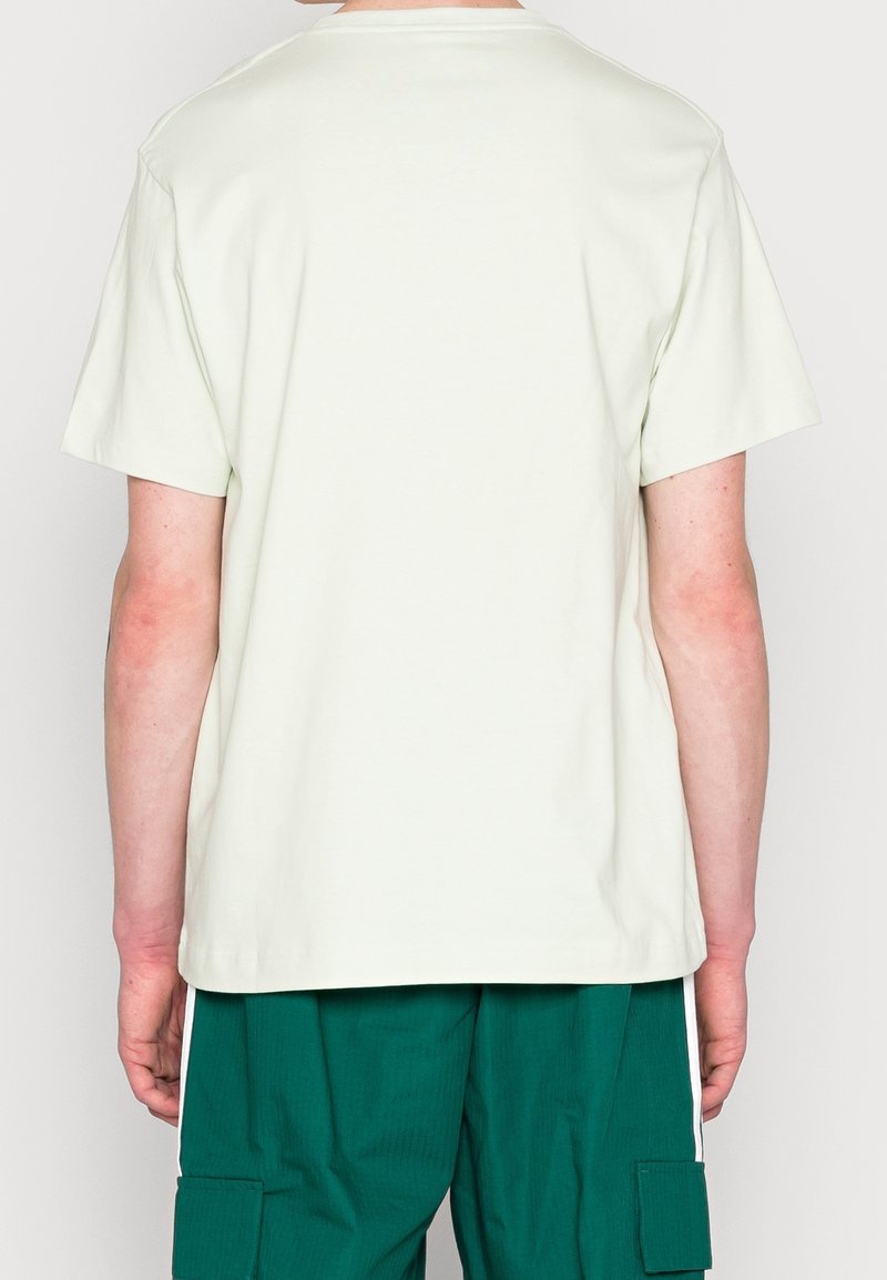 Vue de dos d'une personne portant un t-shirt uni écru à manches courtes et un pantalon cargo vert avec poches latérales.
