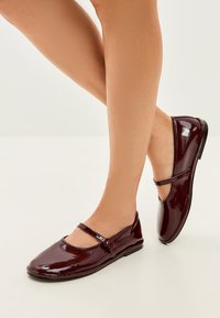 Bordeauxfarbene Lacklederschnürschuhe mit einer runden Zehenpartie und einem dekorativen Riemen über dem Spann, mit einer glatten, glänzenden Oberfläche.