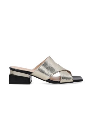 Metallic gold open-toe slide sandal with crisscross design, black block heel, smooth texture, and a flat, shiny black sole.