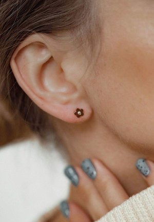 Gold flower stud earring with a central white gem, set against skin. Notable detail includes textured design and small size.