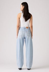 Jeans a gamba larga di colore blu chiaro, realizzati in denim, con vita alta, cuciture visibili e tasche posteriori con un'etichetta in pelle brandizzata.