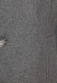 Grijze wollen jas met een gestructureerd, viltachtig oppervlak, voorzien van een metalen knoop aan de linkerkant en subtiele stikdetails.