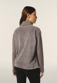 Sudadera de forro polar gris con cuello alto, mangas largas y textura suave. Presenta un reverso liso y un corte relajado.