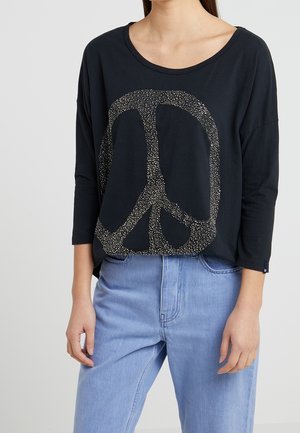 Czarna koszulka z długim rękawem z dużym znakiem pokoju wykonanym z małych kropek. Miękki materiał, luźny krój, okrągły dekolt. Stworzona do noszenia z jasnoniebieskimi dżinsami.