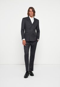Mørk grå dobbeltspent dress med notklapper og sidelommer. Slim-fit bukser og svarte sko. Glatt tekstur, moderne design.