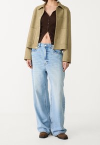 Grön mockajacka, brun ribbad crop top och ljusblå vida jeans. Outfiten har tryckknappar och en avslappnad passform.