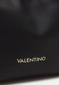 Sac à main en cuir noir texturé avec un logo "VALENTINO" doré sur le devant, présentant une surface lisse et tactile ainsi qu'un design structuré.