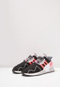 Black mesh athletic shoes with gray accents, pink stripes, and a white heel counter. Features a textured upper and contrasting sole.