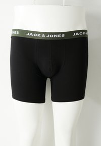 Schwarze Boxer-Shorts für Männer mit olivgrünem Bund, der weißen Schrift "JACK & JONES" zeigt, auf einem weißen Mannequim vom Bündchen abwärts präsentiert.