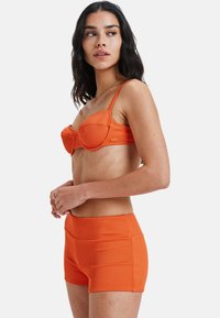 Narancssárga bordázott bikini felső, alátámasztott kosarakkal és állítható pántokkal, párosítva illő, magas derekú sortokkal. Sima textúra és testhez simuló dizájn.