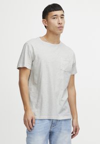 Tricou scurt cu mâneci, gri deschis, cu un model pistruiat, având un decolteu rotund și un buzunar mic pe piept. Este purtat cu blugi albaștri deschiși.