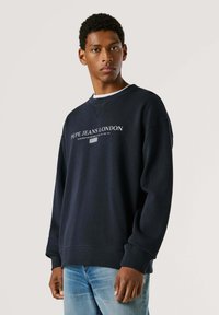 Tumesinise värviga pusa ümar kaeluse, soonikuga varrukaotste ja alaosaga. Esiküljel valge "Pepe Jeans London" logo. Kandmiseks helesiniste teksade peal.