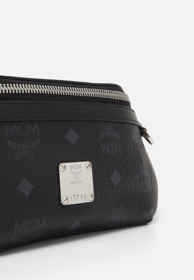 Pochette in pelle nera con texture, zip argentata, loghi MCM impresso e una placca metallica argentata incisa con "MCM München" e un numero di serie.