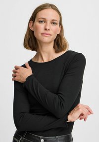 Crna dug sleeves ribana majica s okruglim izrezom i nabranim manžetama, nosi je manekenka s kosom do ramena, na jednobojnoj pozadini.