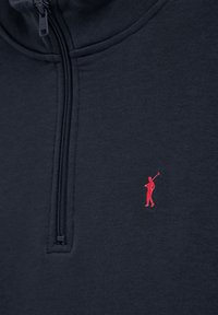 Námořnická mikina s vysokým límcem, zipovým zapínáním a červeným logem golfisty. Měkká textilie, která zvýrazňuje minimalistický design.