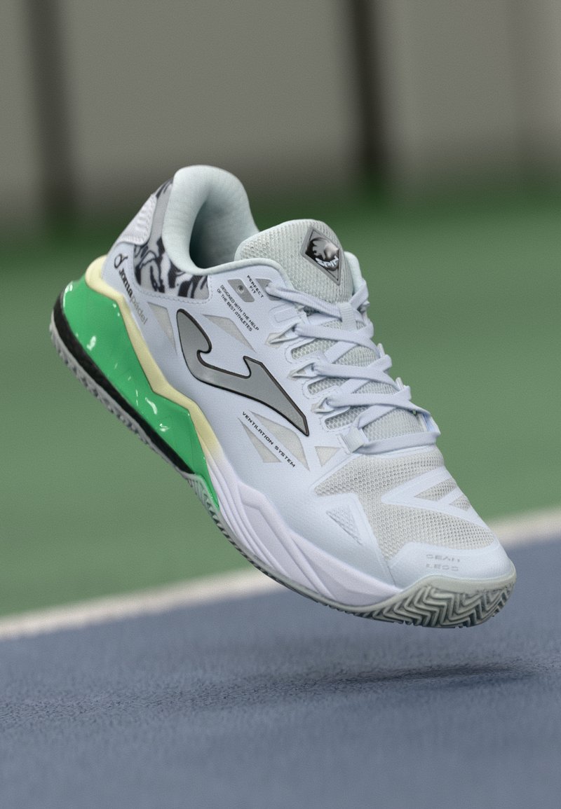 Chaussure de sport blanche avec des accents verts et noirs, tige en maille texturée et talon à motifs. Présente un design épuré et une marque visible.
