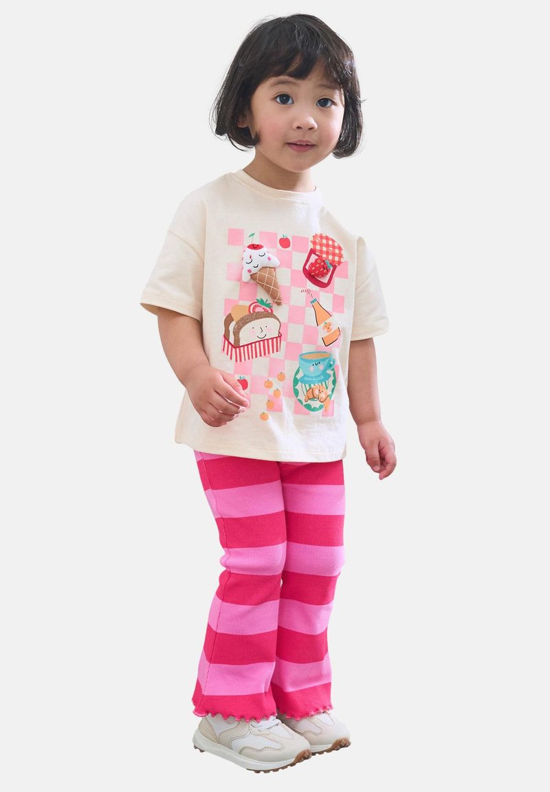 Beige T-shirt met korte mouwen en kleurrijke voedselillustraties op een geruit achtergrond, gecombineerd met felroze en lichtroze gestreepte broek.