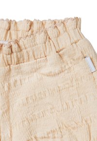 Perzikkleurige gestructureerde stof met een gekreukeld effect, voorzien van een elastische tailleband en een klein geweven label aan de zijkant.