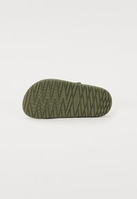 Green rubber shoe sole with a textured zigzag pattern and ventilation holes, featuring a curved shape and logo detail.