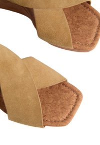 Sandali in suede beige con cinturini incrociati, una soletta in sughero e una punta quadrata. Dettagli cuciti lungo i bordi.