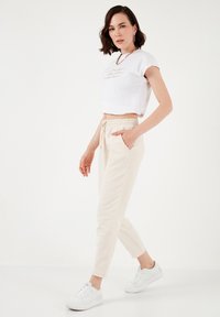 Lightweight, cropped white t-shirt with short sleeves featuring text, paired with beige elastic waist pants, and white sneakers.