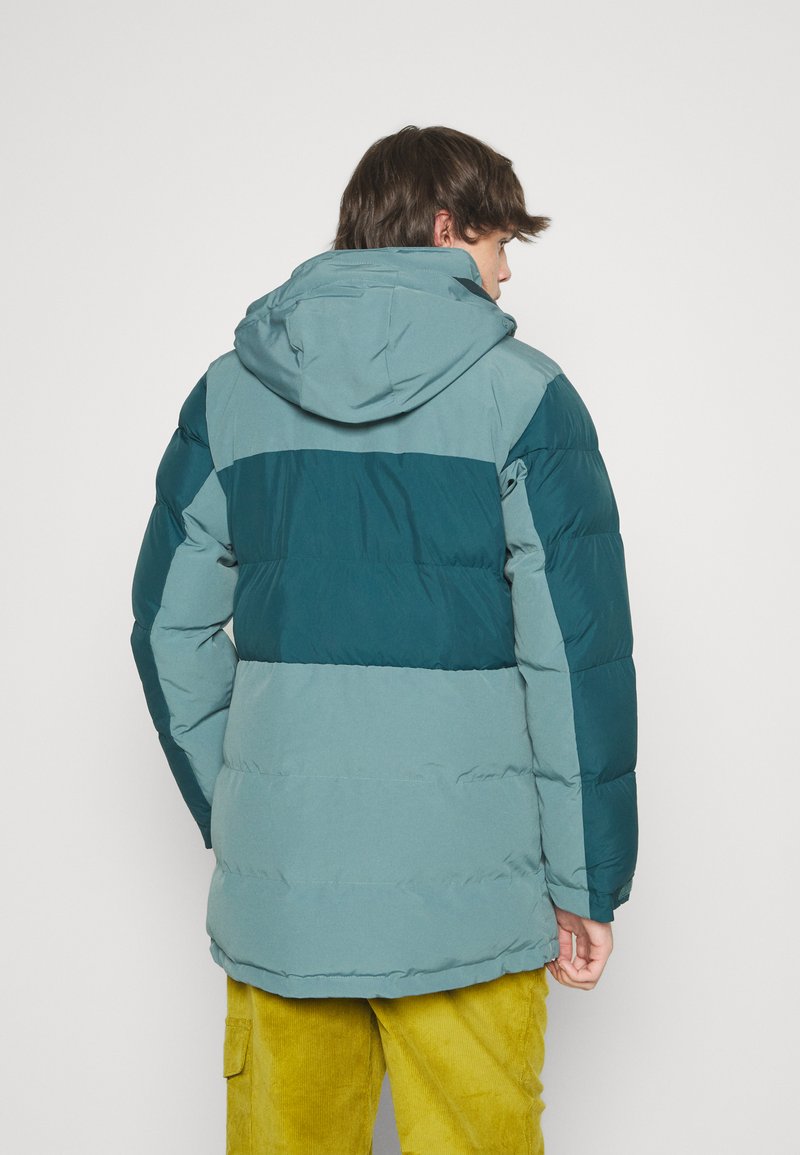 Veste matelassée en teal et bleu clair, dotée d'une capuche, d'un design coloré et de poignets élastiques. Coupe décontractée avec une texture lisse.