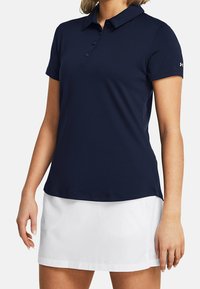 Marinblå pikétröja med krage, tre-knappsstängning och korta ärmar. Tillverkad av mjukt, elastiskt tyg. Vit kjol under.