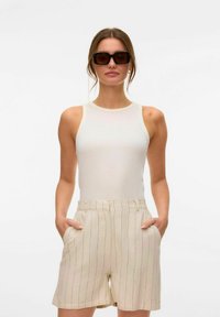 Vit ribbad linne kombinerat med beiga randiga shorts med fickor. Modell som bär mörka fyrkantiga solglasögon. Minimalistisk design.
