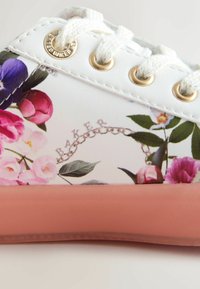 Sneaker bianca con stampa floreale in rosa, viola e verde. Occhielli dorati, suola rosa chiaro e logo decorato con dettaglio a catena.