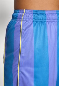 Lilla og blå stribede trænings shorts med elastisk talje, prydet med gule sidestykker og en glat, let stofstruktur.