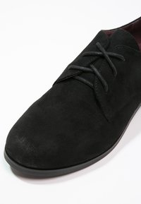 Chaussure habillée en cuir nubuck noir avec un bout rond, une semelle plate et des lacets. Présente une surface légèrement texturée et un design minimaliste.
