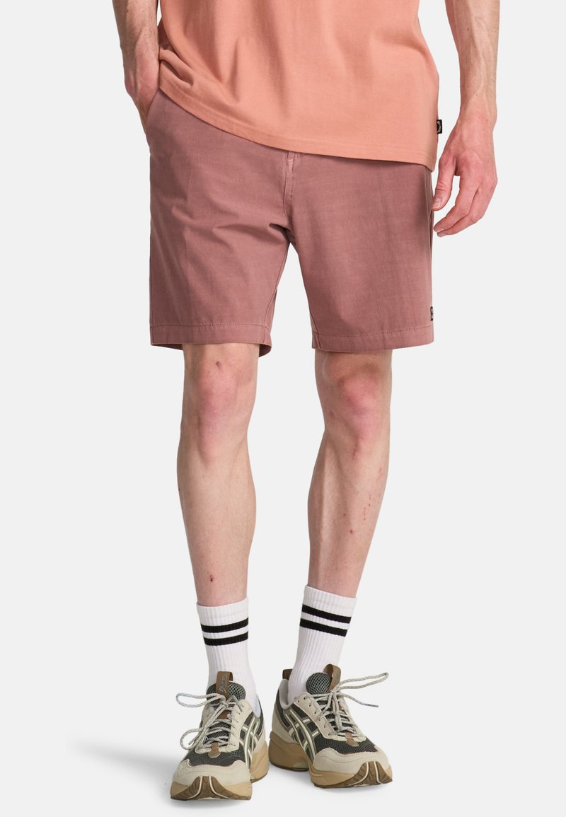 Shorts courts rose pâle en tissu mélange coton, avec une coupe décontractée et des poches latérales. Portés avec des chaussettes blanches à rayures noires et des baskets.