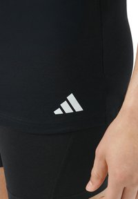 Black athletic shirt with short sleeves, featuring a white Adidas logo on the hem. Close-up shows fabric texture and cut.
