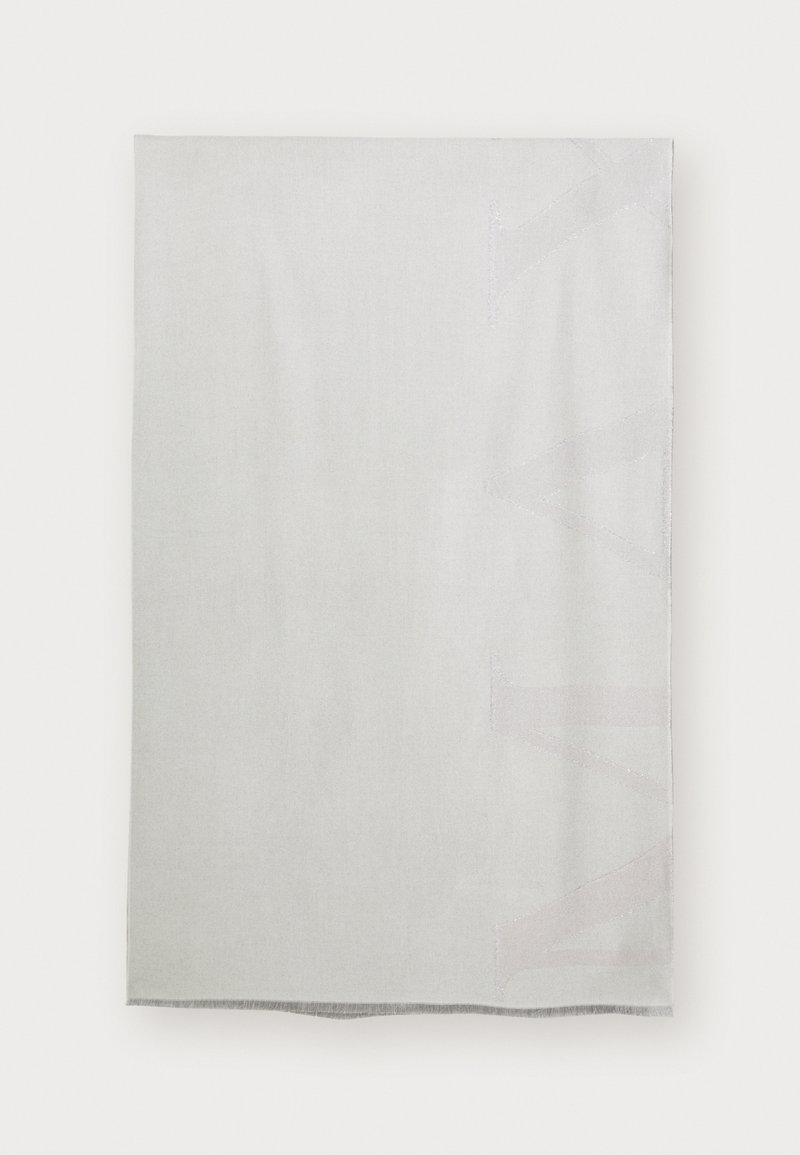 Gaiši pelēka sega ar gludu tekstūru, ar smalku atstarojošu logotipa rakstu vienā stūrī un pušķotiem malām.