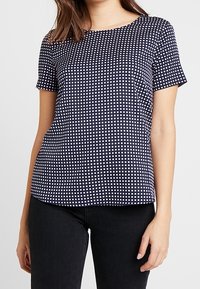 Haut bleu marine à manches courtes avec un motif à carreaux blancs. Présente un col rond et une coupe droite, fabriqué dans un tissu léger.