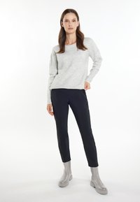 Pulover tricotat gri deschis cu mâneci lungi, asortat cu pantaloni negri tapered. Ținuta este completată cu bocanci gri lucioși până la gleznă.