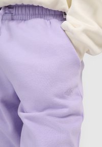 Pantalon de jogging lavande avec taille élastique porté avec un haut crème à manches longues, main dans la poche, petit logo brodé sur la cuisse.