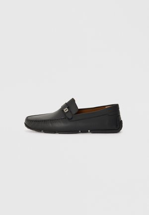 Black leather moccasin-style shoe with a rounded toe, stitched detailing, and a decorative strap. Flexible sole for comfort.