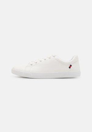 Baltas čības, izgatavotas no gludas materiāla, ar sešām acīm, gumijas zoli un mazu zilu/sarkanu/baltu logo uz papēža. Zema profila dizains.