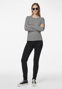 Zwart-wit gestreepte lange mouw top, zwarte skinny jeans en zwarte sneakers met witte zolen. Model draagt donkere zonnebril.