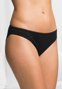Bas de bikini noir en coton avec une coupe taille basse, texture lisse et ceinture élastique étroite. Positionné sur un fond neutre.