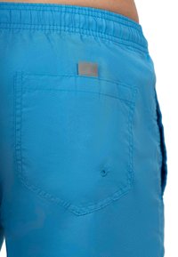 Pantaloni da bagno blu realizzati in tessuto leggero, con una tasca sul retro dotata di una linguetta grigia e un piccolo dettaglio di cucitura decorativa.