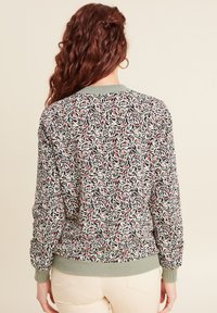 Gemustete Bomberjacke mit floralem Design in Schwarz, Weiß und Rot, ausgestattet mit einem grünen gerippten Kragen und Bündchen sowie einem elastischen Taillenbund.