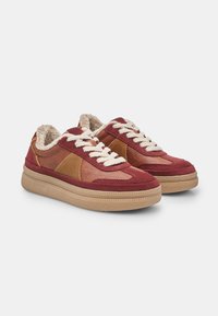 Červené a hnedé kožené tenisky s huňatým interiérom, textúrovanou gumovou podrážkou a béžovými šnúrkami. Obsahujú prekrývajúci sa dizajn panelov a detaily prešívania.