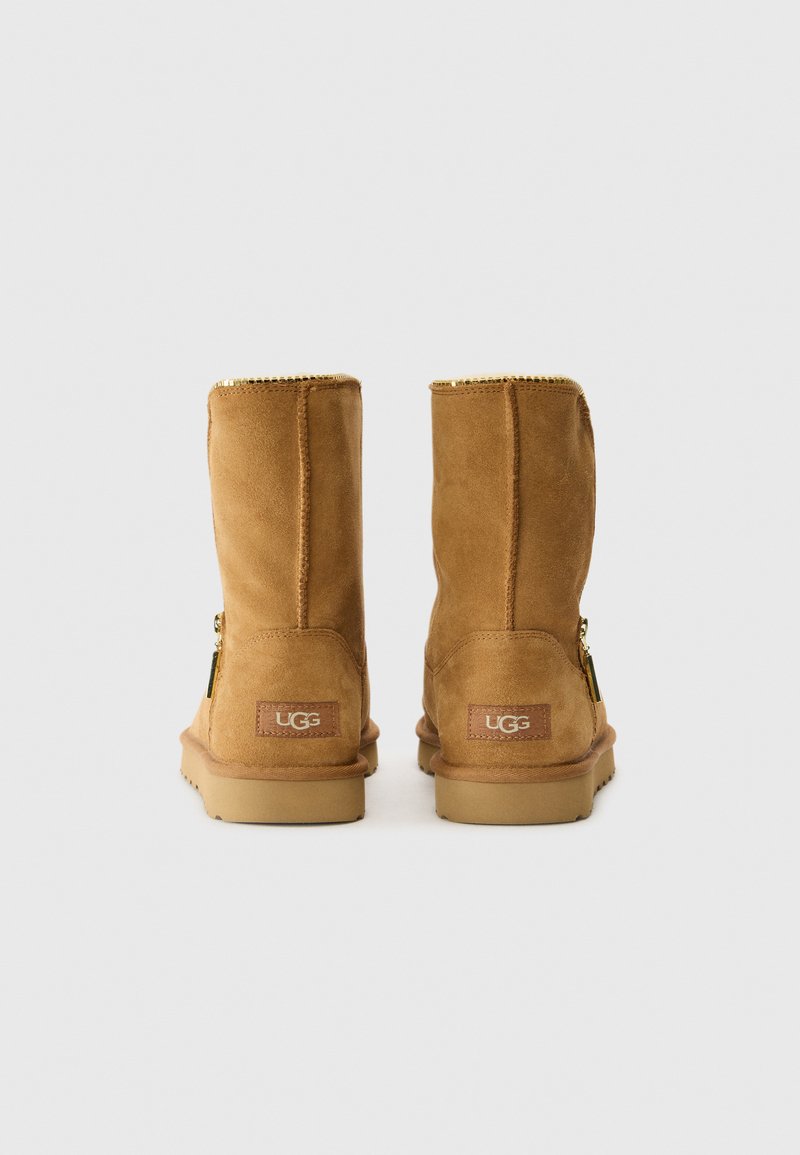 Helle Wildleder-Stiefeletten mit glatter Textur, goldfarbenem Reißverschlussdetail und Gummisohle. Mit einem kleinen Logopatch auf der Rückseite.